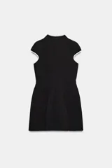 Vestido corto negro con cuello mao, abertura en el pecho y ribetes blancos en contraste. Cuenta con mangas cortas y cierre lateral con cremallera oculta.