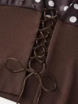 Top asimétrico negro con lunares blancos, con un hombro descubierto y detalle de elástico en la cintura.