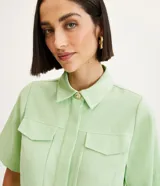 Camisa color verde claro de crepé, con cuello camisero, abotonado delantero, mangas cortas y solapas delanteras aplicadas.