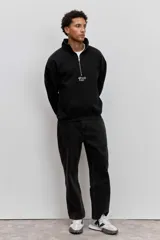 Buzo de cuello alto con cierre frontal parcial, de corte holgado y diseño minimalista con pequeño estampado central en el pecho.