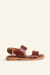 Sandalias planas de cuero vacuno color marrón, con diseño de tiras anchas en el empeine, sujeción en el talón con hebilla metálica ajustable y suela de cuero con bajo tacón.