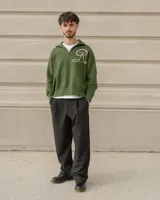 Sweater tejido de algodón en color verde oscuro, con cuello alto y cierre frontal parcial. Presenta un diseño de letra R bordada en color beige en el frente.