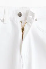 Jean blanco de denim de algodón rígido, corte baggy con tiro alto, piernas holgadas de silueta curva y diseño de cinco bolsillos.