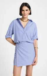 Vestido camisero corto de algodón en color celeste con finas rayas blancas, con diseño asimétrico tipo wrap, mangas largas y escote en V con cuello camisero.