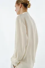 Camisa de manga larga confeccionada en seda 100%, con cuello mao y cierre frontal con botones. Presenta un diseño con bajo asimétrico y puños clásicos.