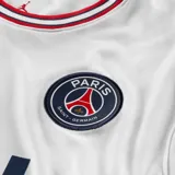 Camiseta de fútbol Nike del Paris Saint-Germain, modelo Stadium Home. Diseño blanco con detalles en azul marino y rojo en cuello y mangas. Incluye logo de Nike, escudo del club y sponsor ALL en el frente.