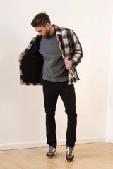 Campera de estilo camisa confeccionada en tela de lana a cuadros en tonos gris, negro y blanco. Presenta cierre frontal con botones, cuello clásico y bolsillos frontales.