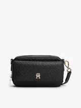 Cartera estilo camera bag negra, estructurada y compacta, con textura integral de monograma TH en relieve y placa metálica dorada con el logo TH en el frente. Posee cierre superior y correa ajustable para llevar al hombro o cruzada.