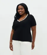 Blusa Ashua confeccionada en viscolycra, de color negro, con escote en V, mangas cortas y detalle de ribete ondulado en contraste en el cuello.