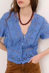 Camisa azul de manga corta confeccionada en tejido broderie con diseño calado y floral. Cuenta con escote en V y cierre frontal de botones.