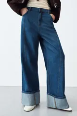 Jeans de tiro alto con corte wide leg, confeccionados en denim azul. Presentan diseño de cinco bolsillos, cierre frontal con cremallera y botón, y bajo con vuelta ancha.