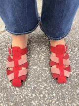Suecos tipo sandalias franciscanas elaborados en cuero, con tiras entrelazadas de gamuza en tonos rojo, rosado y bordó. Cuentan con una hebilla metálica lateral y suela plana.