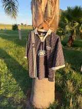 Polo de manga corta con cuello tipo polo y escote en V, corte boxy fit. Presenta un patrón texturizado en relieve y un logo ovalado con la inscripción "with love" en el pecho.