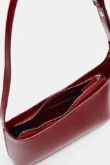 Bolso de hombro rojo de diseño asimétrico en acabado brillante. Cuenta con asa ajustable, bolsillo interior y cierre mediante cremallera metálica.
