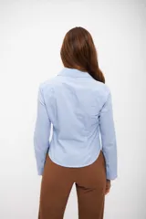 Camisa de manga larga, color celeste claro, con finas rayas verticales blancas. Presenta cuello camisero y calce entallado.