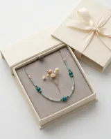 Collar de acero con baño de oro, compuesto por una delicada cadena de pequeñas cuentas en tonos celestes y verdes, intercaladas con piedras naturales redondas de mayor tamaño en color turquesa y verde oscuro.