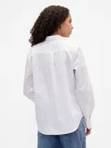 Camisa de manga larga color celeste, con cuello clásico, cierre frontal de botones, bolsillo en el pecho con detalle bordado y dobladillo redondeado.