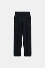 Pantalón tobillero de tiro alto con pliegues delanteros, bolsillos laterales y bajo con vuelta. Presenta cierre frontal con cremallera, botón y gancho.