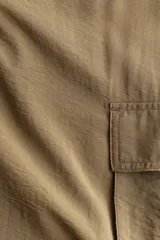 Pantalón cargo de tejido liviano color verde militar, con cintura elástica y cordón ajustable. Presenta diseño de piernas holgadas y bolsillos laterales con solapa.