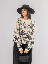 Sweater de punto con calce oversized, fondo color crudo y diseño estampado de flores en color negro. Presenta cuello redondo y mangas largas.
