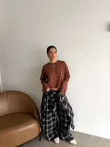 Remera de manga larga color marrón, con cuello redondo y detalle de parche cuadrado con logo bordado en el centro del pecho. Presenta un corte holgado y diseño minimalista.