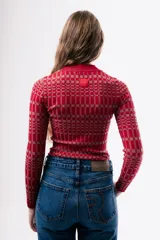 Top de punto ajustado al cuerpo, con cuello redondo y manga larga. Presenta un diseño de estampado geométrico a cuadros en tonos rojos y rosados.