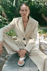 Blazer sastre de corte recto, color beige, con cuello solapa, hombreras marcadas y cierre frontal de dos botones oscuros. Cuenta con bolsillos con solapa en el frente y un bolsillo ojal en el pecho.