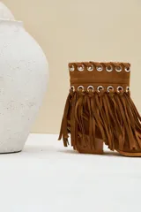 Bota texana de gamuza color camel, con taco cuadrado y punta fina. Cuenta con flecos largos colgantes y detalles de ojalillos metálicos plateados en la parte superior.
