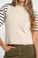 Chaleco de punto sin mangas en color beige melange con motas oscuras. Presenta cuello redondo y terminaciones acanaladas en el ruedo y las sisas.