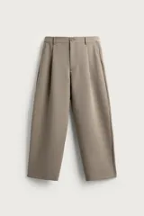 Pantalón de vestir relaxed fit color beige, con pliegues frontales, bolsillos laterales y cierre de cremallera y botón.