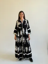 Vestido largo negro con estampado floral blanco, escote en V con cuello mao, cierre frontal de botones y mangas tres cuartos acampanadas.