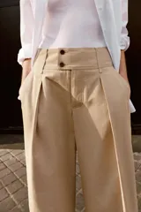 Pantalón de tiro bajo con pinzas delanteras, bolsillos frontales y bolsillos de plastrón con solapa en la parte trasera. Presenta una pernera ancha y bajo con botones a presión para ajuste.