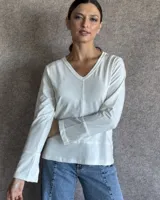 Remera de manga larga color blanco con cuello en V. Presenta costuras decorativas visibles en el centro, en el escote y en los puños, con un diseño de corte recto y acabado sencillo.