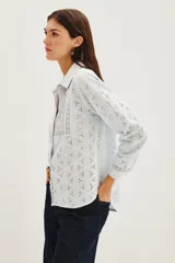 Camisa de algodón con diseño de encaje bordado, cuello clásico y frente con tablas verticales. Presenta mangas largas con puños abotonados y cierre frontal con botones.