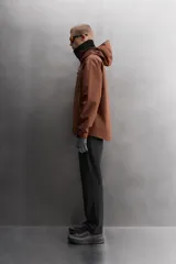 Cazadora deportiva color marrón confeccionada en tejido técnico de tres capas con membrana impermeable. Cuenta con cuello alto con capucha ajustable, mangas largas con puños reforzados ajustables, aberturas con cremallera en axilas, bolsillos frontales con cremallera y bajo ajustable con elásticos laterales.