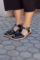 Sandalias de cuero negro con diseño de tiras entrecruzadas, hebilla dorada y suela plana.