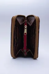 Billetera marrón tipo sobre con cierre de cremallera, confeccionada en cuero con textura tipo cocodrilo y forro textil rojo. Cuenta con múltiples ranuras para tarjetas, documentos y billetes.