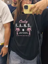 Remera oversize marrón con estampado gráfico frontal en tonos celestes y blancos con la leyenda "Only Fans", palmeras y estrellas.