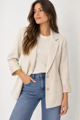 Blazer de corte entallado color beige, con solapas de muesca, cierre frontal de dos botones y bolsillos de ojal. Las mangas largas cuentan con vueltas en los puños con estampado de rayas en tonos rosado y verde.
