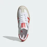 Championes Adidas modelo Samba OG, fabricados en cuero blanco con las icónicas tres tiras y detalles en rojo solar, puntera de nobuk gris claro y suela de goma marrón.