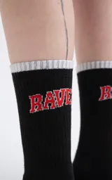 Medias 3/4 de algodón color negro, con el texto 'RAVERS' bordado en rojo en la parte superior y logo 'LUXO' en la planta del pie. Presentan un borde superior acanalado en color gris claro.