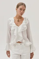 Blusa blanca de gasa con lunares, escote en V con volados y mangas largas acampanadas.