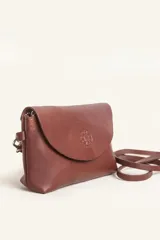 Cartera tipo sobre de cuero color marrón, con solapa frontal redondeada que presenta un detalle circular grabado. Incluye correa larga ajustable y extraíble, cierre principal y broche de seguridad.