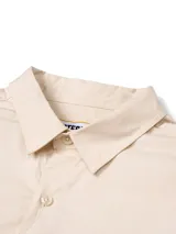 Camisa de manga larga Caterpillar estilo utilitario, color beige, con múltiples bolsillos con solapa en el pecho, detalles de tiras negras y logo de la marca bordado.