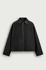 Sobrecamisa relaxed fit color negro, confeccionada en tejido con algodón, con cuello solapa en efecto cuero a contraste, cierre frontal de cremallera metálica y bolsillos de vivo en la cadera.