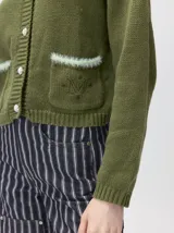 Cardigan de algodón grueso color rojo, con cuello redondo, cierre frontal de botones grandes y bolsillos cuadrados en el frente. Presenta detalles de pelo sintético en el cuello y los bolsillos, y logo bordado en uno de los bolsillos.