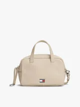 Cartera de mano tipo bowling de Tommy Jeans, color beige, con doble asa superior y correa ajustable extraíble. Presenta un diseño estructurado con cierre superior y logo metálico de la marca en la parte frontal.
