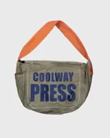 Bolso tipo tote o bandolera de lona color caqui con estampado frontal en azul marino que dice "COOLWAY PRESS". Posee una correa ancha de tela color naranja brillante y detalles en cuero marrón.