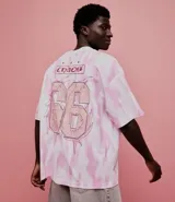 Remera oversized de algodón con teñido tie-dye en blanco y rosa. Presenta un cuello redondo y un estampado frontal con la palabra "Chaos" y un diseño de llamas en color rosado.