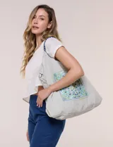 Bolso tote amplio color beige, con cordón de ajuste superior, asas de cordada trenzada bicolor y detalle de bolsillo con bordado central de diseño paisley en tonos azules.